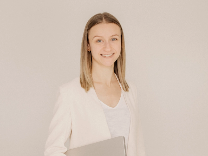 Leonie-Rieder-Webdesign-mit-WordPress-3 Leonie Rieder, eine junge Frau mit dunkelblonden Haaren, hat ein Laptop unter dem Arm und lächelt freundlich in de Kamera. Sie trägt ein weißes Oberteil und einen hellbeigen Blazer.