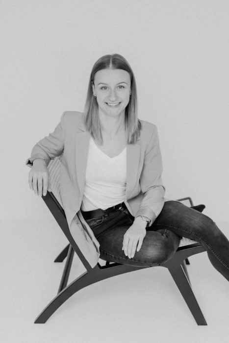Leonie-Rieder-WordPress-Webdesignerin Leonie Rieder, eine junge Frau mit dunkelblonden Haaren, hat ein Laptop unter dem Arm und lächelt freundlich in de Kamera. Sie trägt ein weißes Oberteil und einen hellbeigen Blazer.