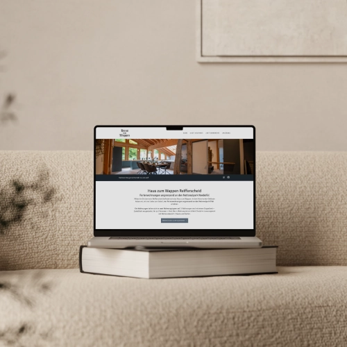Mockup-Website-FerienwohnungenReifferscheid Laptop auf einer hellen Couch mit der geöffneten WordPress Website der Ferienwohnungen im Haus zum Wappen in Reifferscheid (Hellenthal, NRW), die ein modernes WordPress Webdesign mit Divi zeigt.
