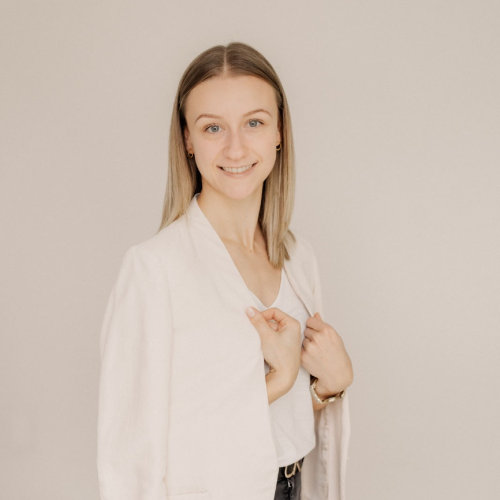 WordPress-Expertin-aus-der-Eifel-Leonie-Rieder Leonie Rieder, eine junge Frau mit dunkelblonden Haaren, hat ein Laptop in der Hand und lächelt freundlich in de Kamera. Sie trägt ein weißes Oberteil, einen hellbeigen Blazer und eine schwarze Hose.